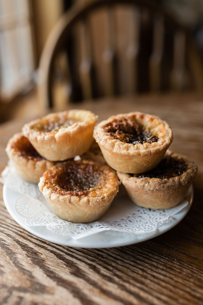 an image of 6 butter tarts stacked on a plate, on a table