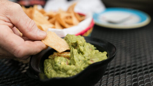 Hand scooping guacamole on a tortilla chip