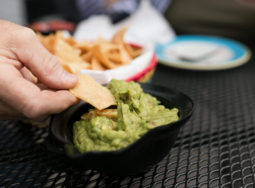 Hand scooping guacamole on a tortilla chip