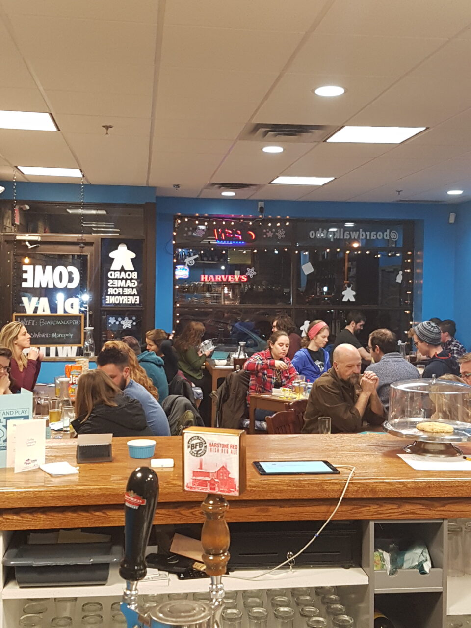 view from the bar of a packed room of people playing board games, eating and drinking