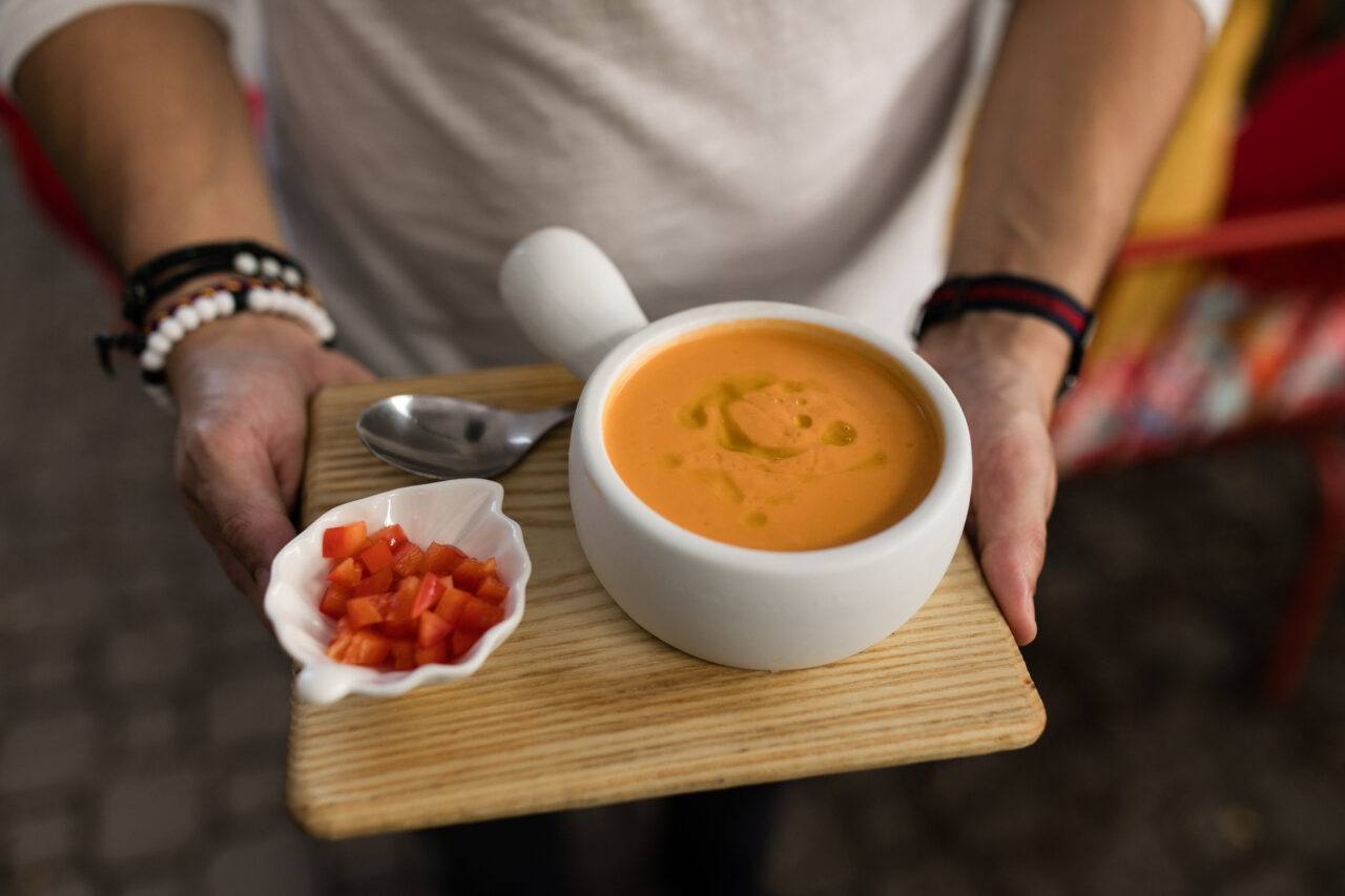hands holding a board with a bowl of soup and chopped peppers