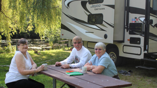 Three seniors sitting at a picnic table in front of an RV