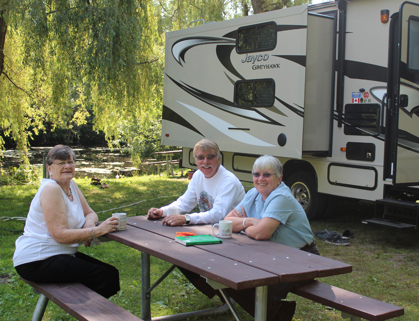 Three seniors sitting at a picnic table in front of an RV