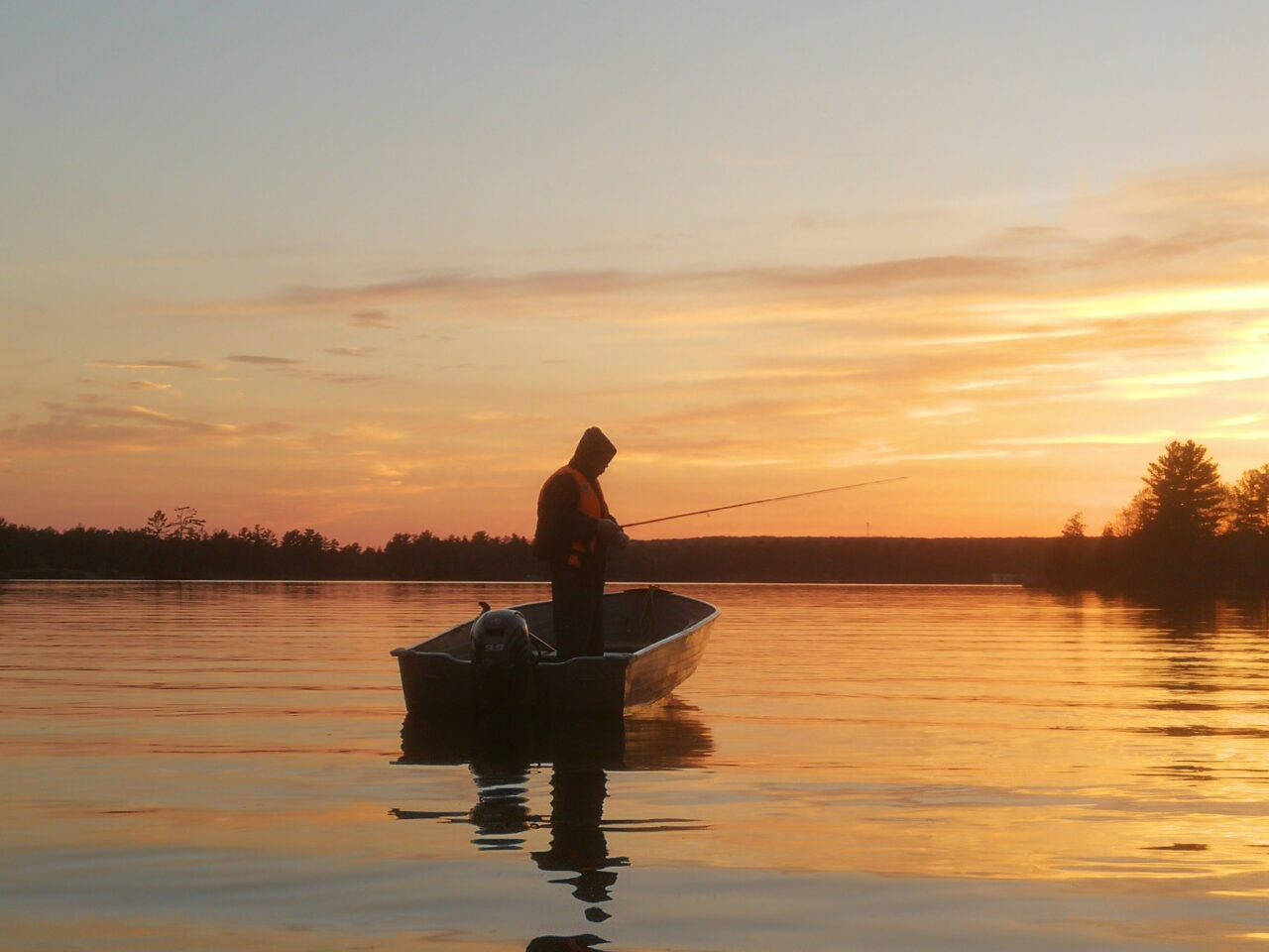 A man fishing from a small boat on a lake at sunset