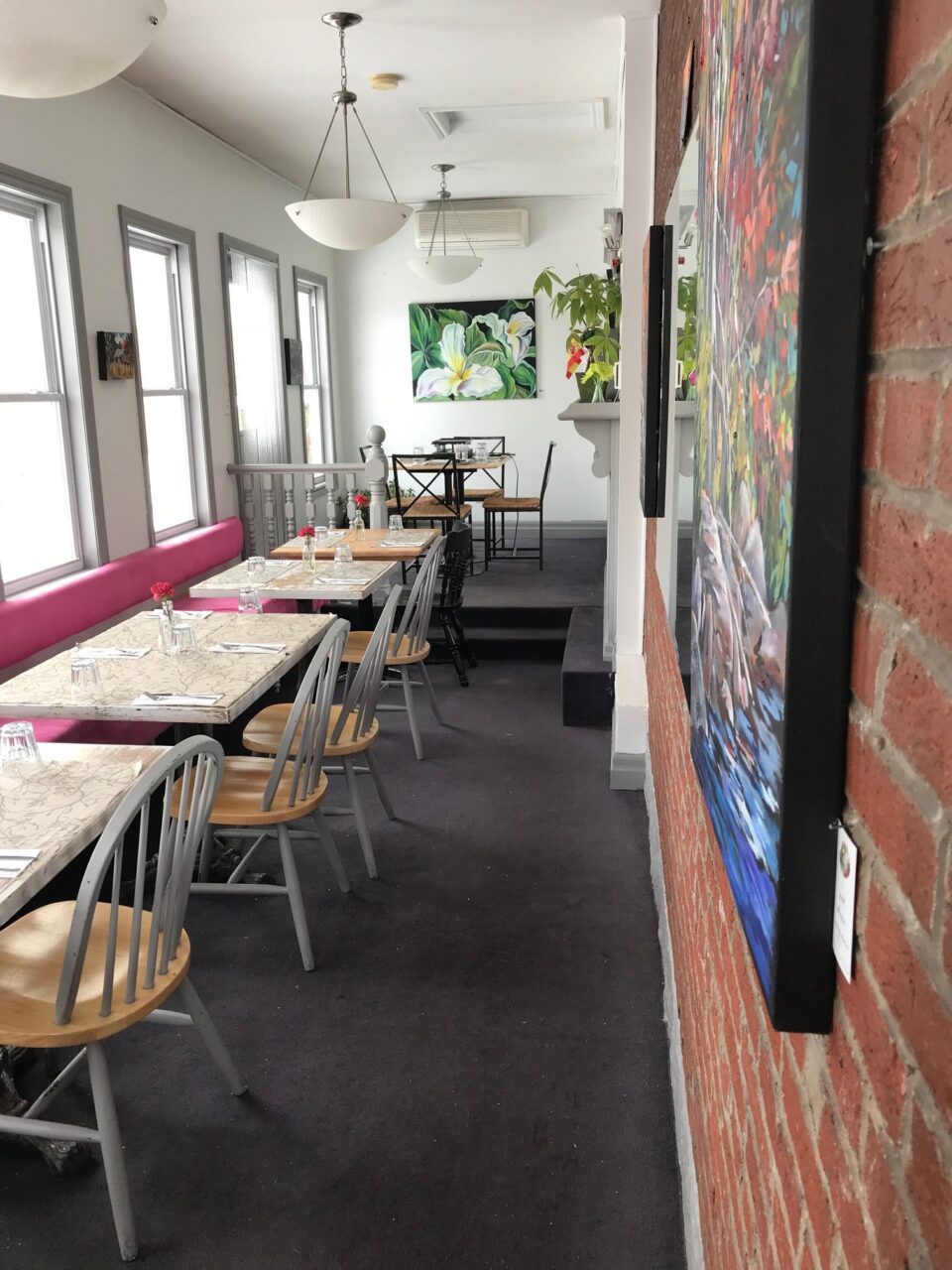 An empty dining room of a cafe with tables and chairs on the left and artwork on the right