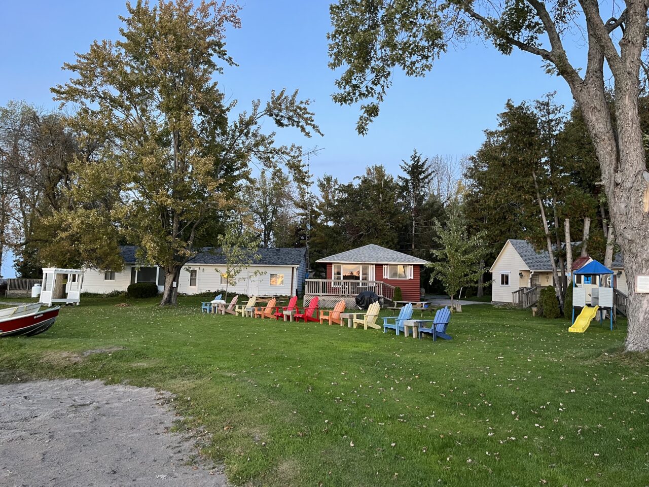View from waterfront looking towards Lakeside Cottages, with a lineup of multi-coloured Adirondack chairs