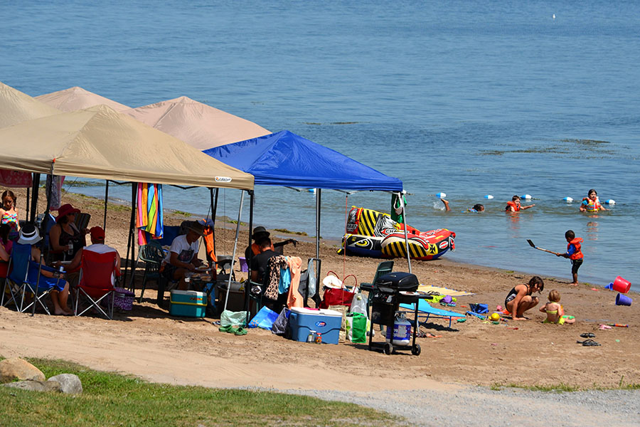 people sitting under tents on the beach while children play
