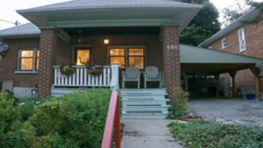 Front of a brick house with 2 chairs on porch