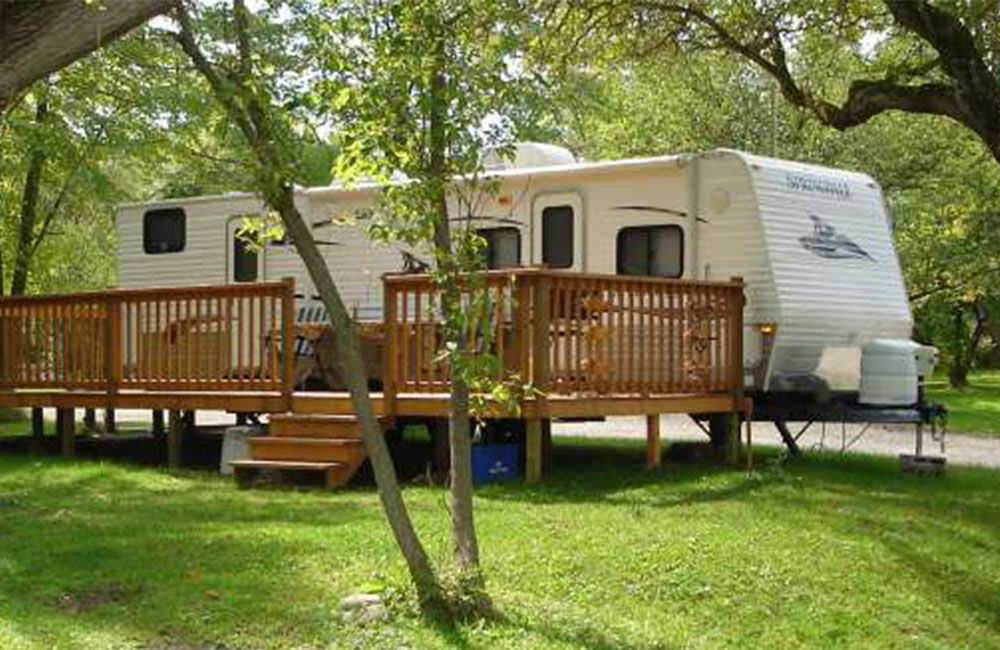 an RV on a green lawn surrounded by trees