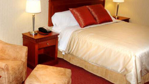 a bed in a hotel room with a yellow comforter, white sheets and red pillows