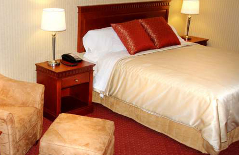 a bed in a hotel room with a yellow comforter, white sheets and red pillows