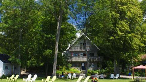 A cottage style resort surrounded by forest, overlooking a large lawn with deck chairs