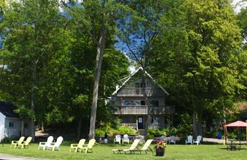A cottage style resort surrounded by forest, overlooking a large lawn with deck chairs