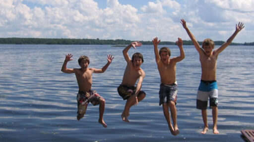4 boys jumping off dock into lake