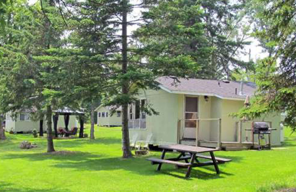a bunch of white cottages with picnic tables on grass with trees