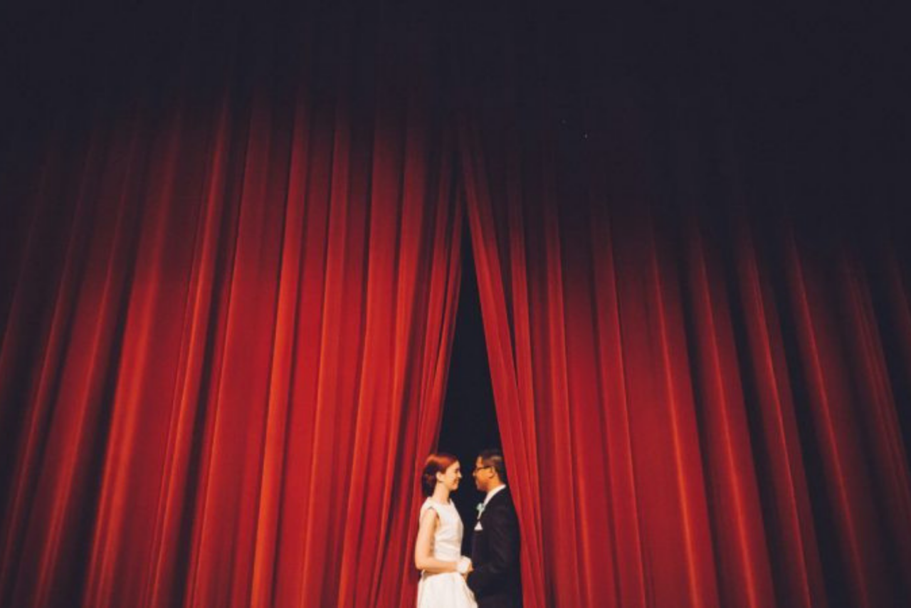 a bride and groom stand between red curtains