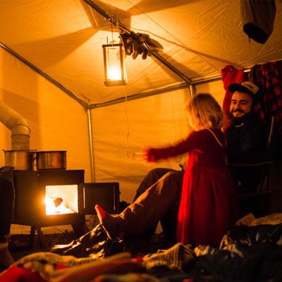 girl pointing at a glowing stove to show it to a man in a camping tent
