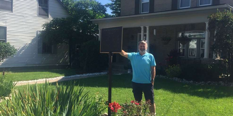man standing by sign infront of house