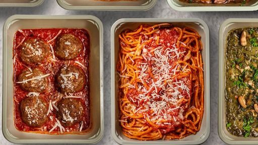 There are many cooking metal pans laid horizontally across and in rows throughout the entire photo. Starting from the top right corner of the photo and following across to the right side is lasangna with pesto, chicken parmesan with pesto, and sliced roasted potatoes. The second row starting from left to right horizontally is 6 large meatballs in a marinanra sauce with parmesan, spaghetti with parmesan, and another pan of food. On the third row there is a corner of a pan of food, chicken thighs in a red sauce, and sauted vegetables.