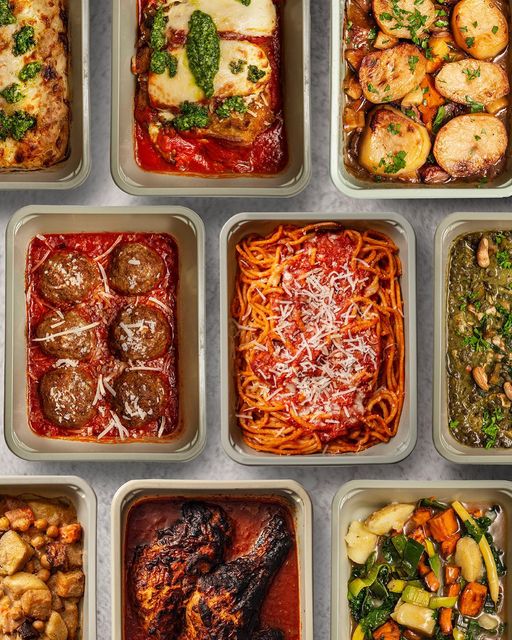 There are many cooking metal pans laid horizontally across and in rows throughout the entire photo. Starting from the top right corner of the photo and following across to the right side is lasangna with pesto, chicken parmesan with pesto, and sliced roasted potatoes. The second row starting from left to right horizontally is 6 large meatballs in a marinanra sauce with parmesan, spaghetti with parmesan, and another pan of food. On the third row there is a corner of a pan of food, chicken thighs in a red sauce, and sauted vegetables.