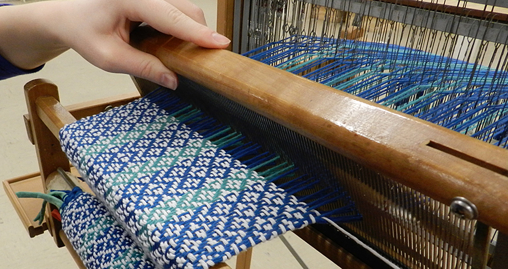 A close up of a person weaving on a loom