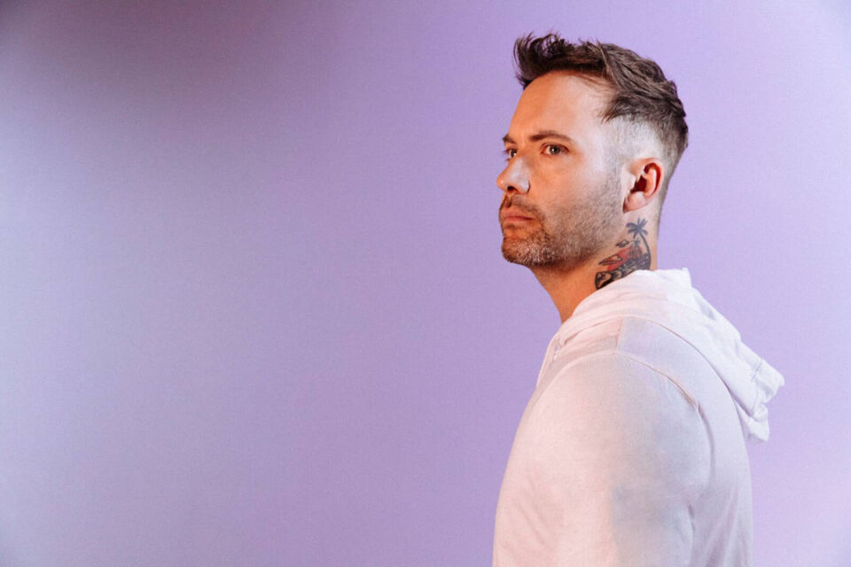 Dallas Smith standing in front of a purple background looking off in the distance
