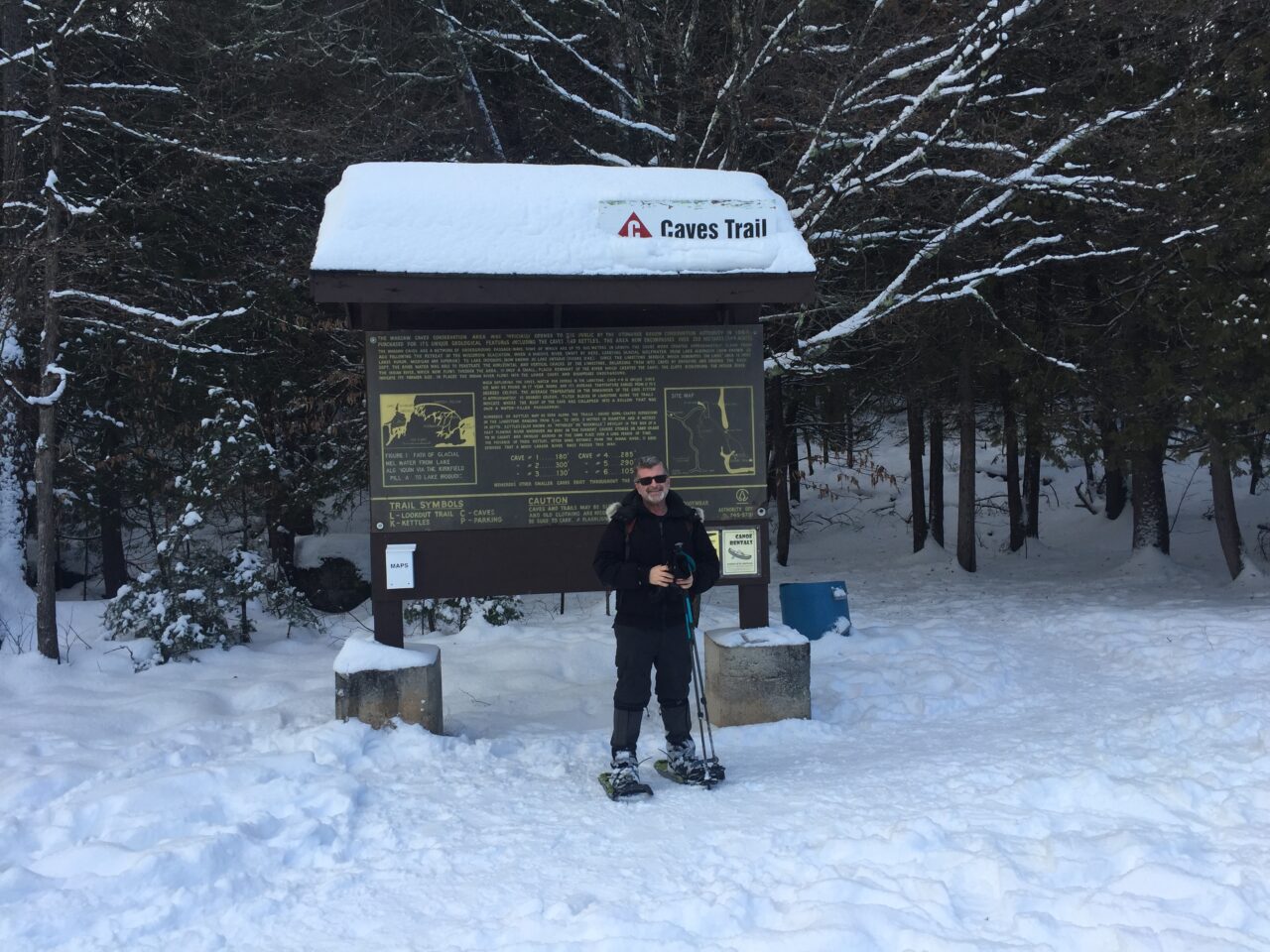 Man snowshoeing in front of Caves trail informational board