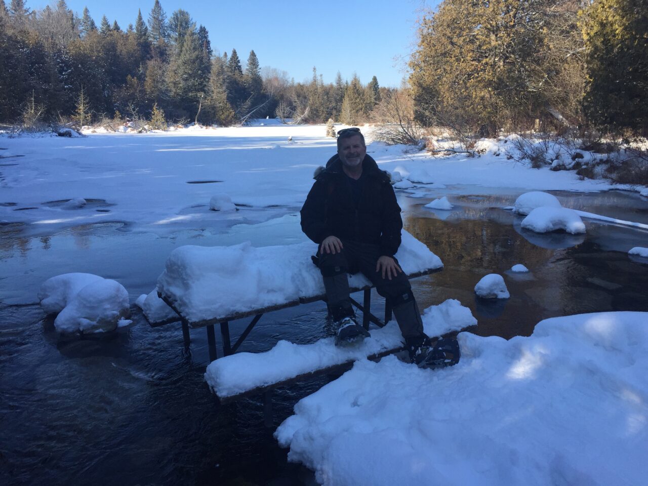 man sitting on a bench covered with ice in a partially frozen pond