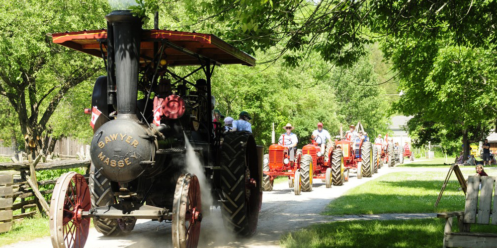 Parade of people riding tractors through a forest