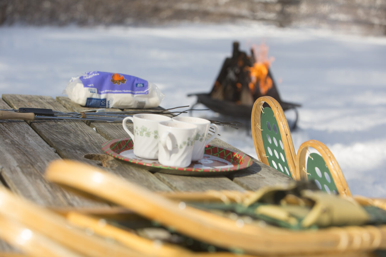 A picnic table with snowshoes and coffee sitting on it
