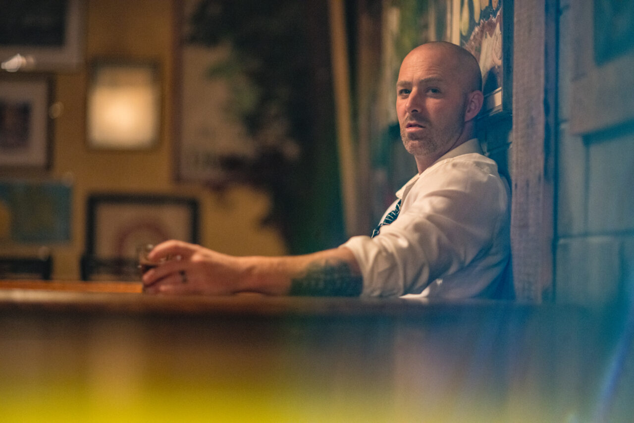 a man sitting in a bar with a drink looking at the camera