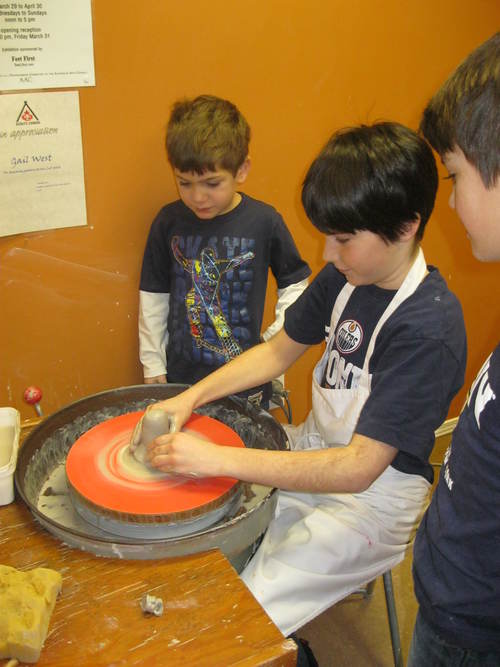 three young boys around pottery wheel one boy turning pottery