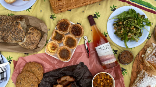 A selection of food and wine lay on a picnic blanket