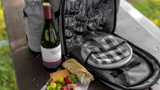 A bottle of wine, a wrap, and wine glasses in a backpack stand on a table.