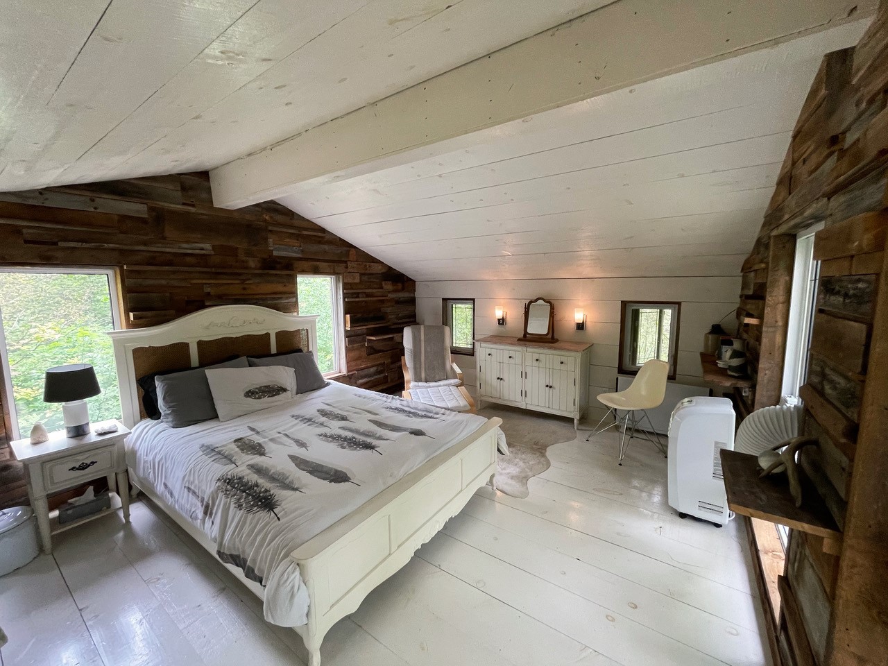 Interior of Ravenswood showing a spacious suite with large, white linened bed and wood accent wall. This is an eco cabin retreat in Trent Lakes Peterborough & the Kawarthas