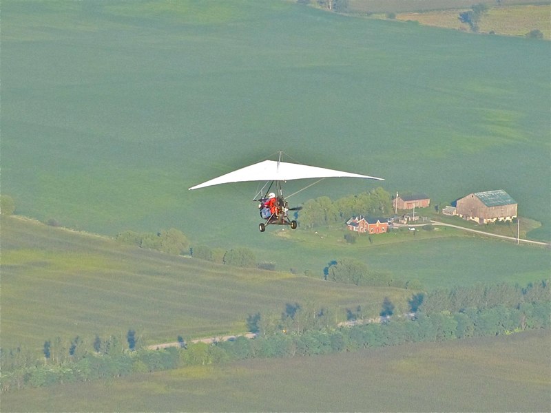 red & white areotrike plane flying with farm house below