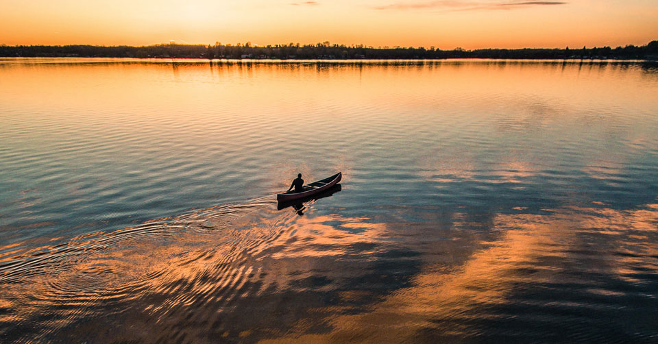 person in a canoe in the middle of a lake at dawn