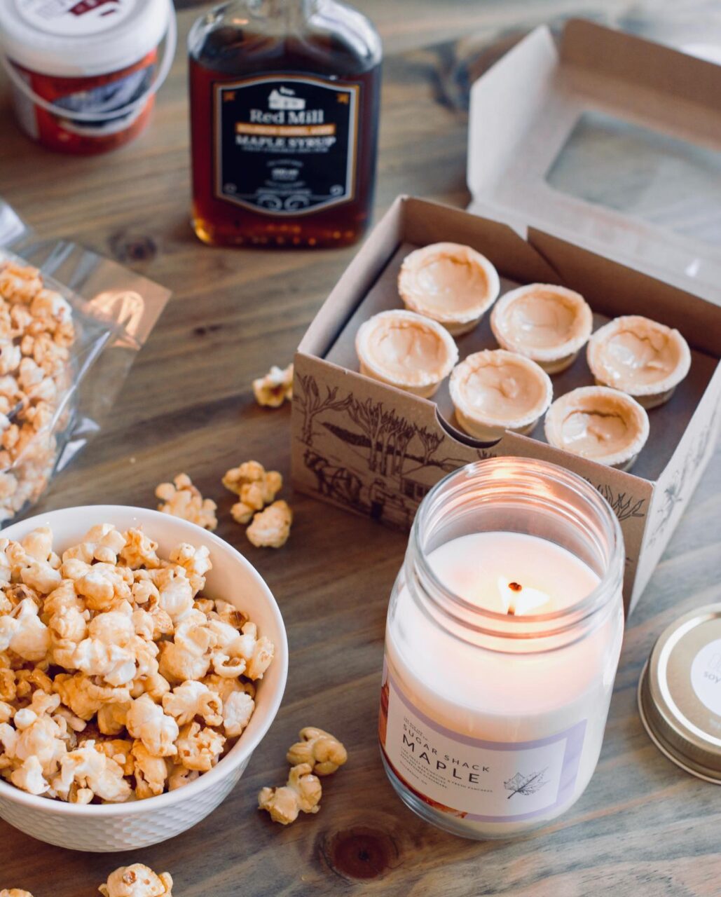 a table with maple syrup, butter tarts, popcorn and a candle