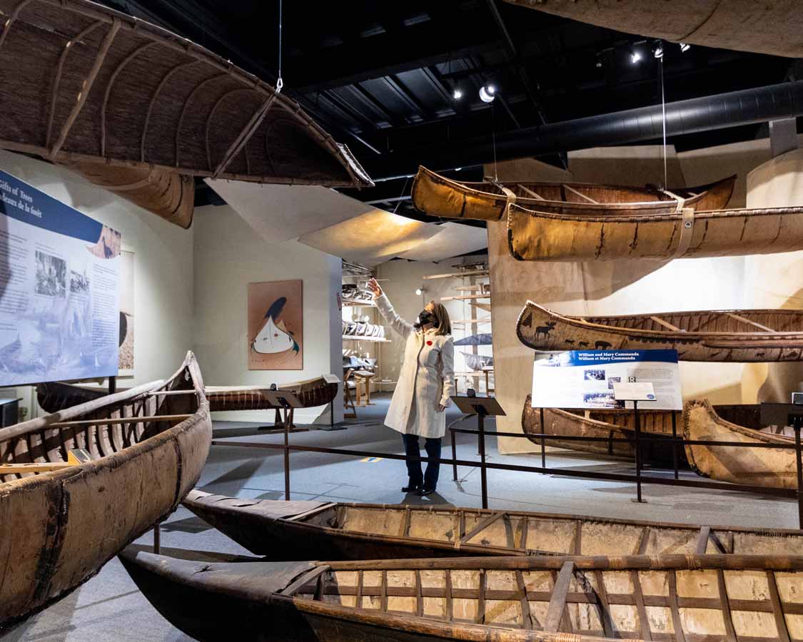 A woman standing in Canadian Canoe Museum pointing upwards at canoe