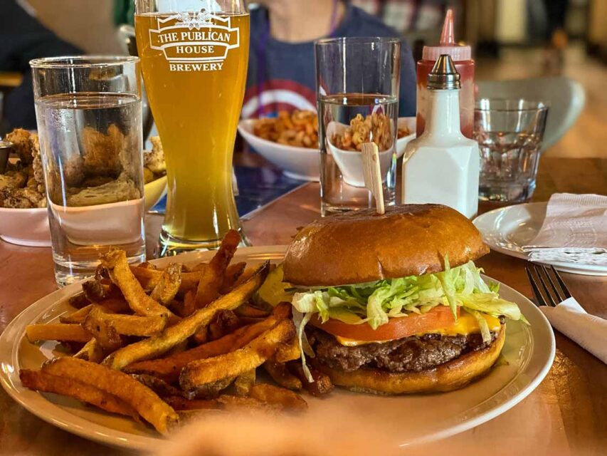 A plate with burger and fries, with a glass of beer and water behind it