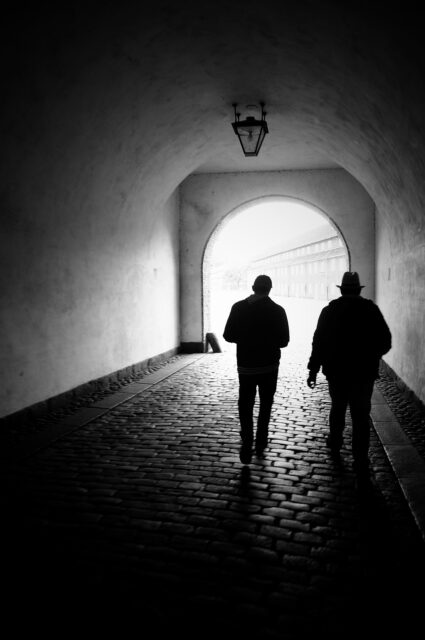 Black and white photo of dark tunnel with two people walking awayt=