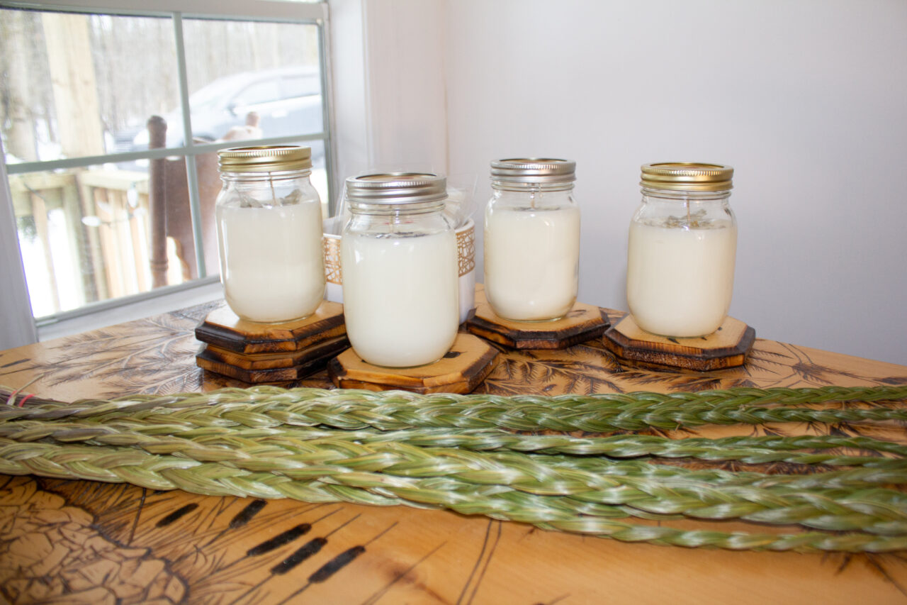 four candles in glass jars with greenery in front