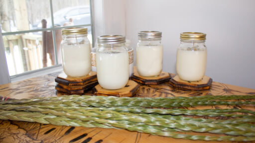 four candles in glass jars with greenery in front