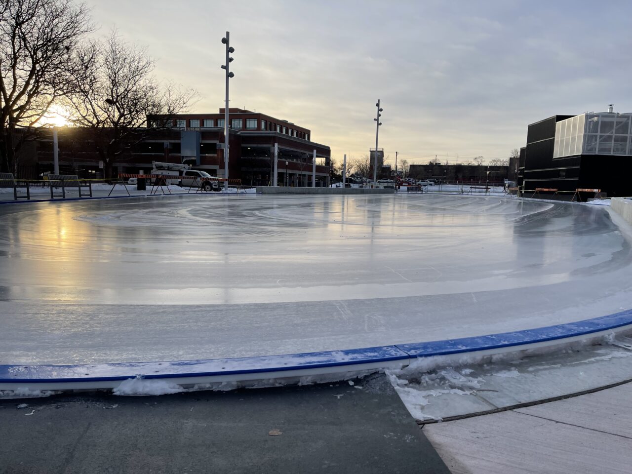 an image of an outdoor skating rink, at dusk, in a downtown setting