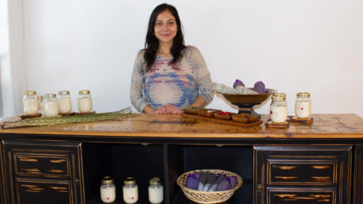 woman standing in front of white wall, behind shelf with jarred candles on top