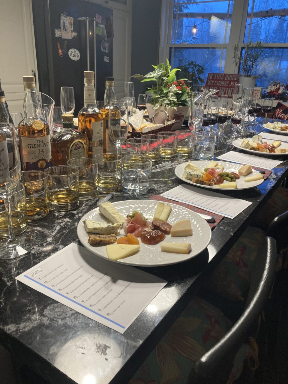 Table filled with tasting menu and whisky pairing items. White plates with small assortment of cheeses and clear glasses with brown liquid (whisky)