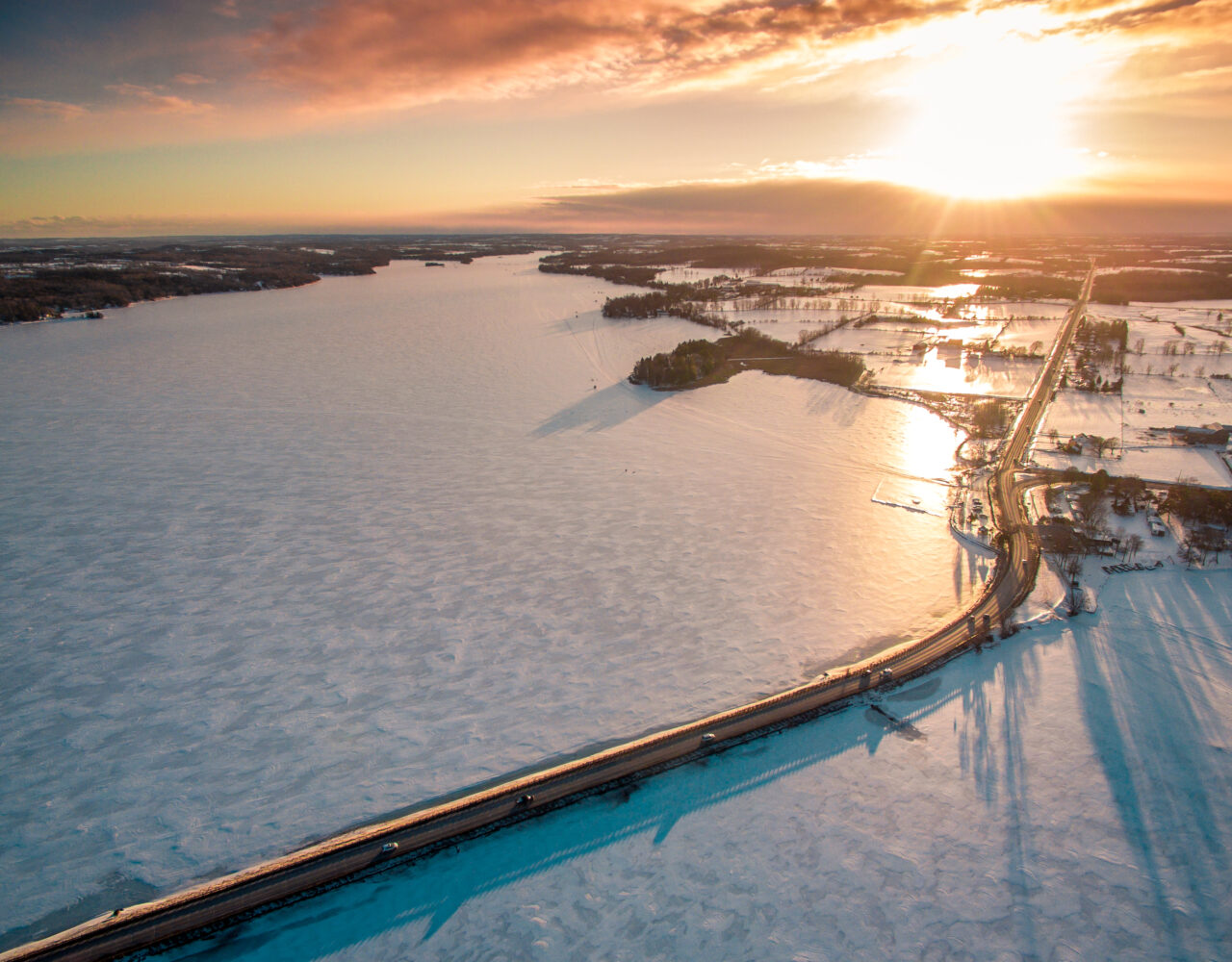 Aerial image of frozen lake with Bridgenorth Causeway in the middle. Sunset in the background