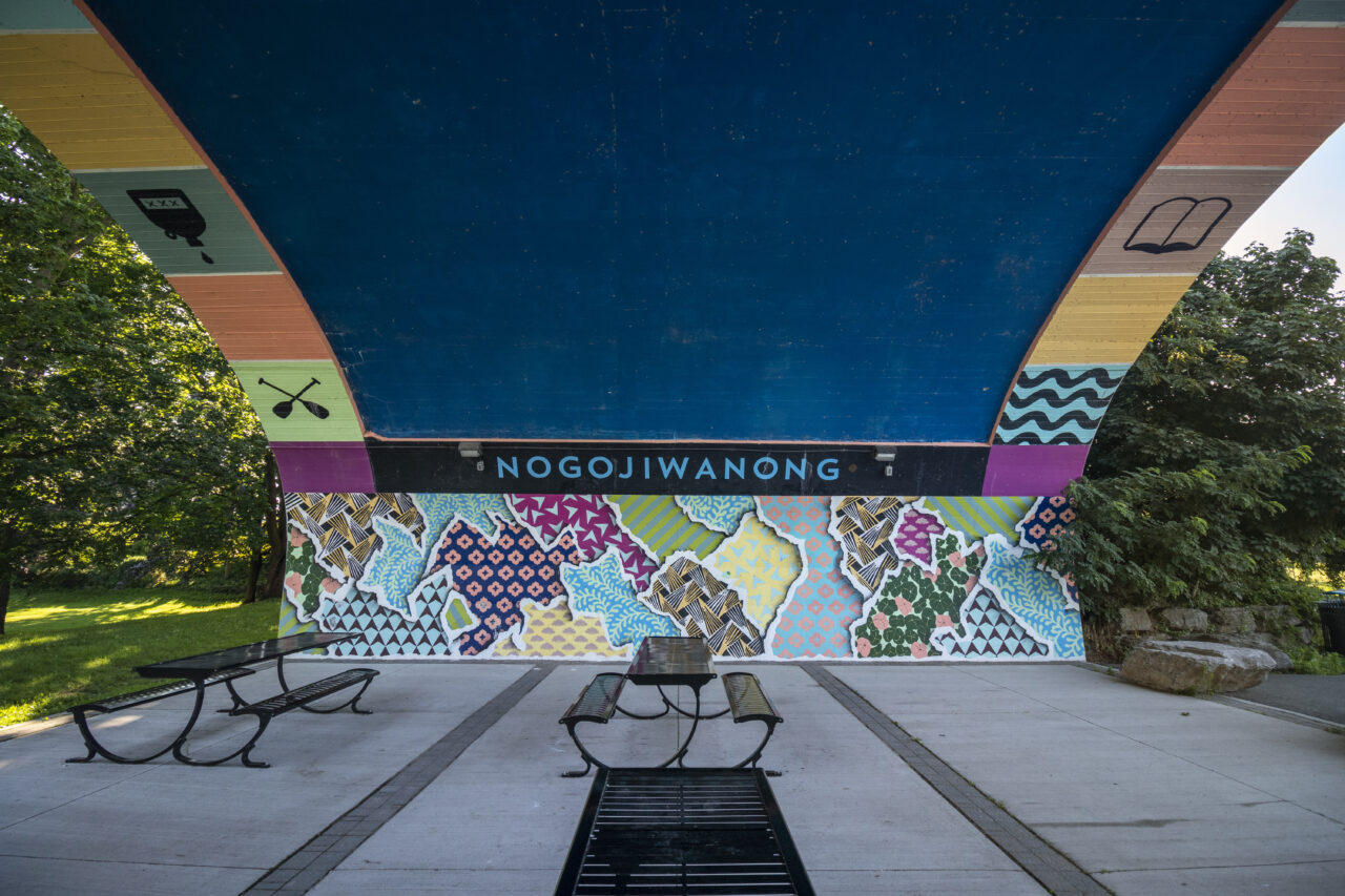 image of Hunter Street Bridge Mural. Colourful background with "Nogojiwanong" written in the middle