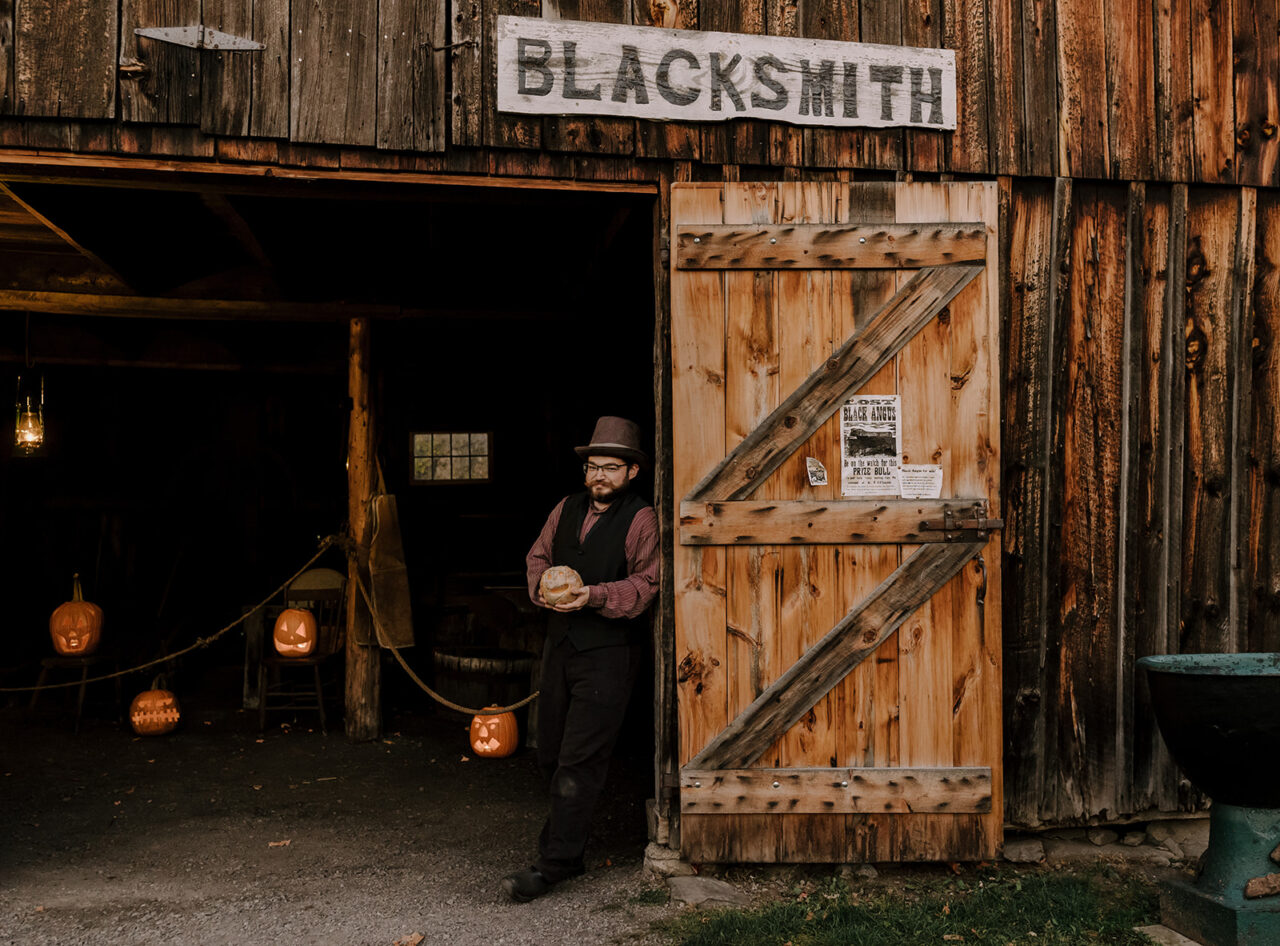 Man stands at the doorway of Blacksmith shop decorated for Halloween.