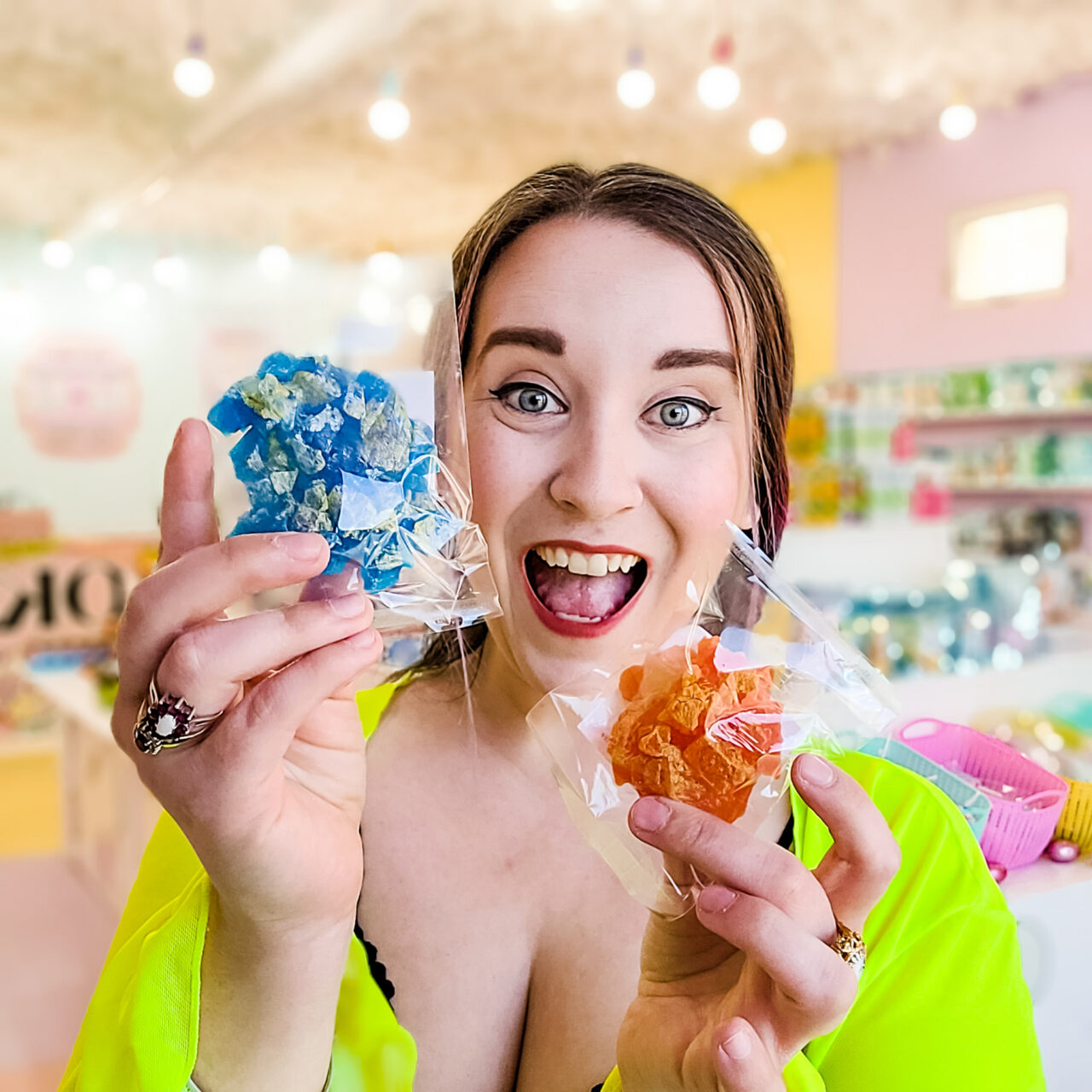Owner Polly smiling holding two bags of candy, in brightly coloured store front.